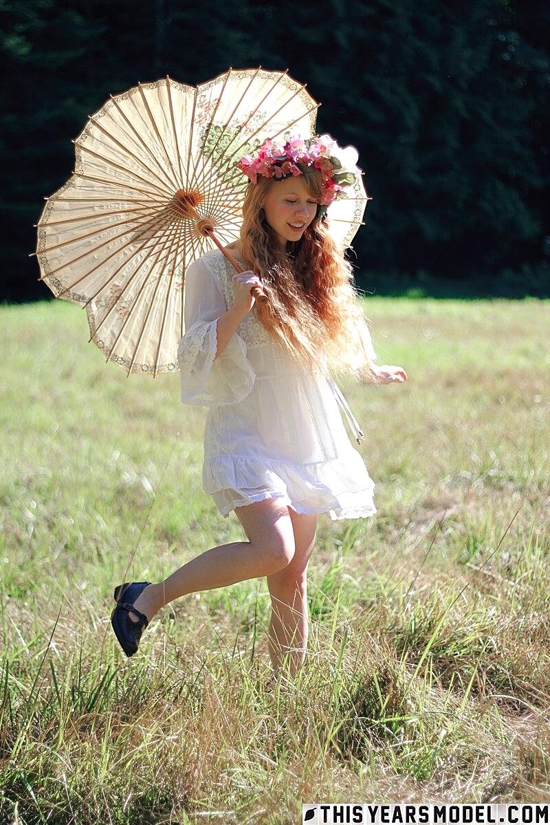 Charming redheaded teen Dolly Little holds a parasol while getting naked
