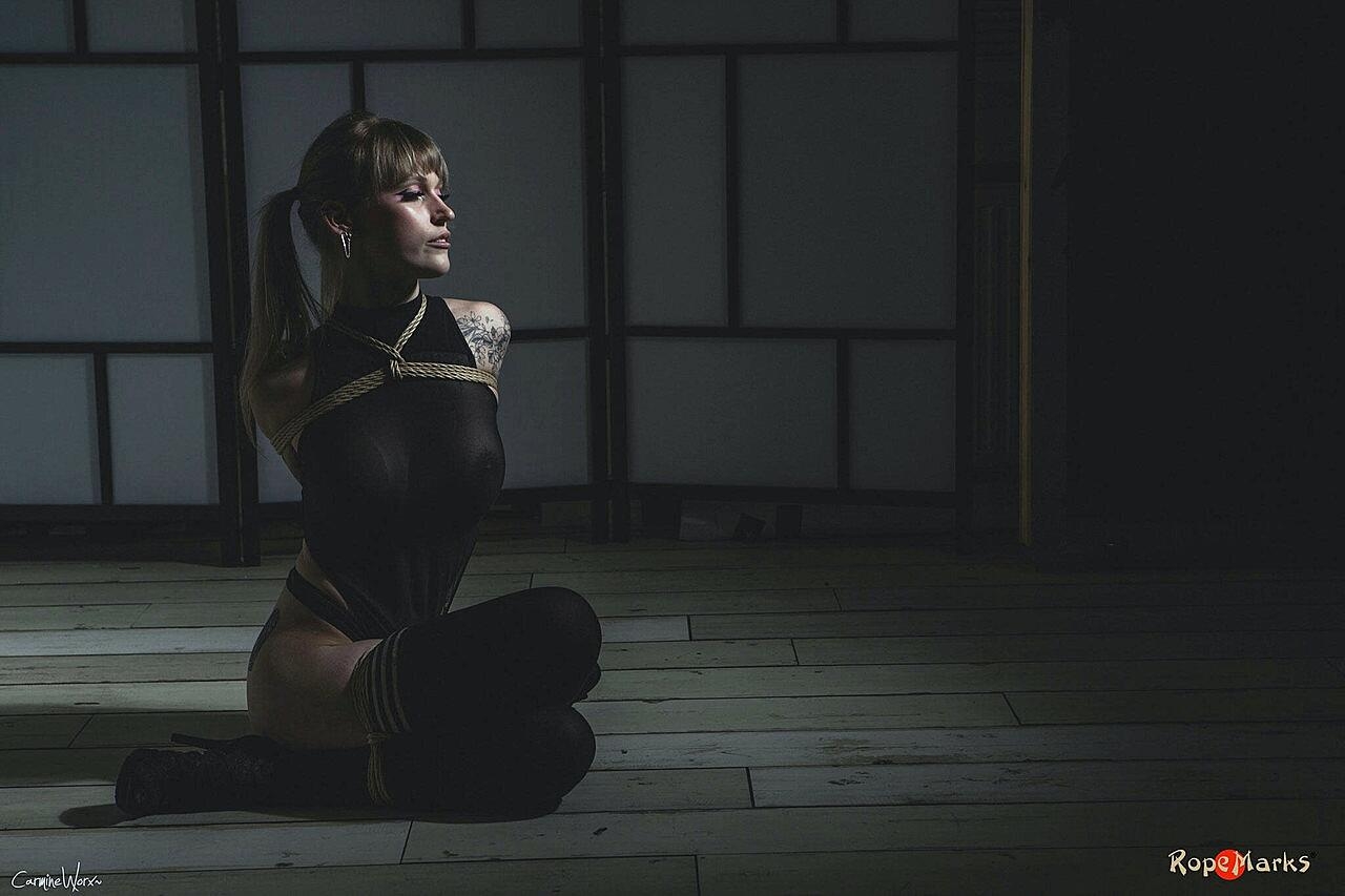 Tattooed blonde Carmine Worx has her arms tied behind her back
