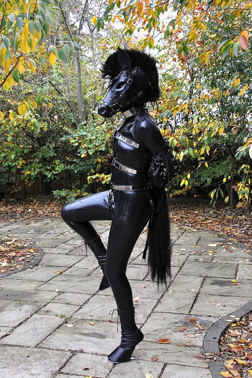 Kinky slut posing outdoors in a horse mask and a full-coverage latex outfit