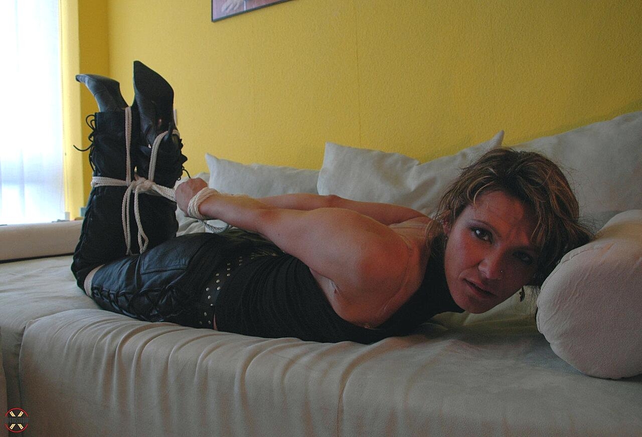 Dirty blonde struggles against a ball gag while hogtied in leather pants